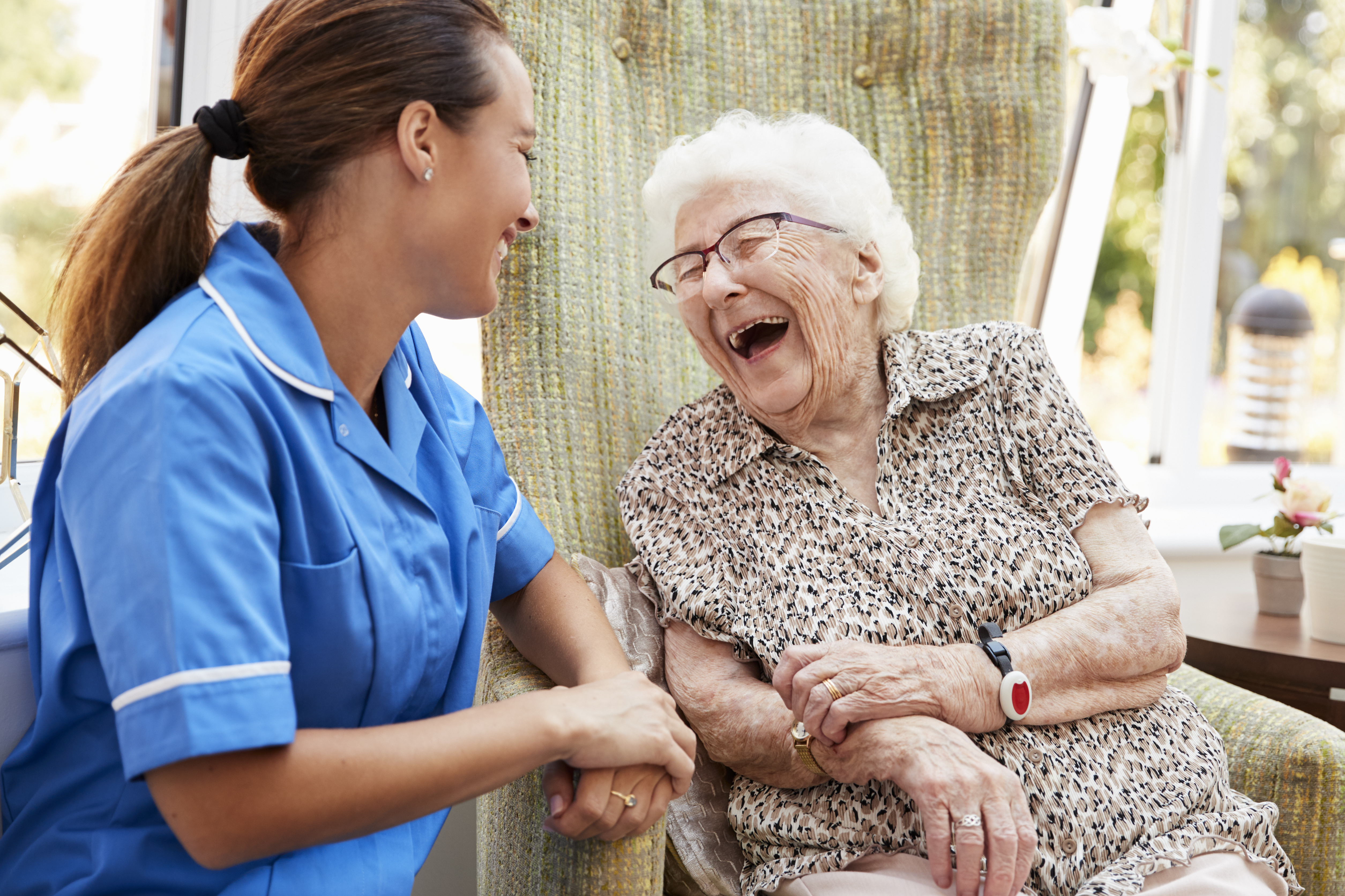 An elderly woman sat in a garden laughing with a care worker.