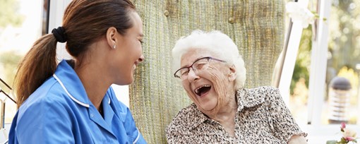 An elderly woman sat in a garden laughing with a care worker.