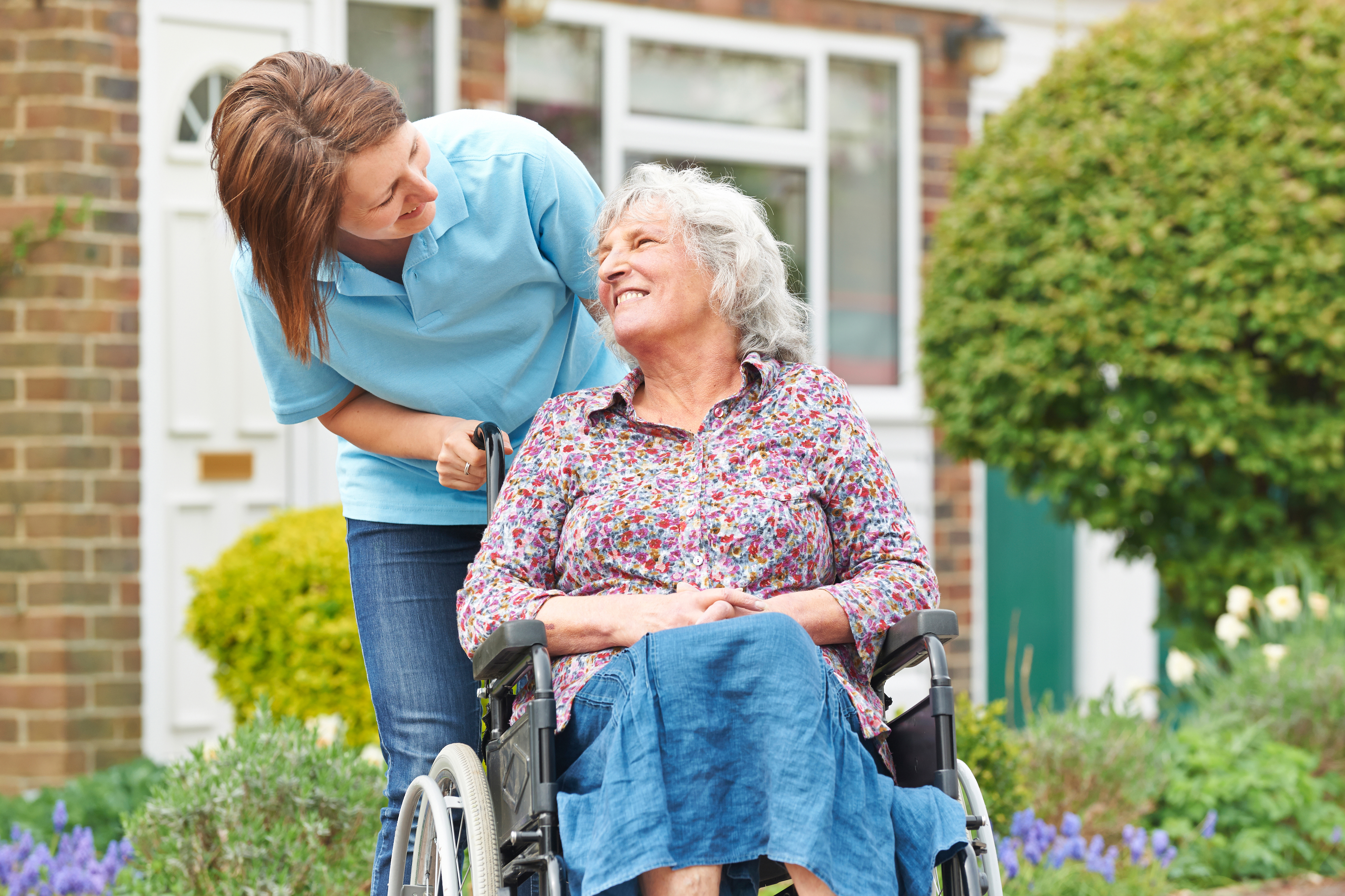 A woman pushes another woman in a wheelchair and they laugh together